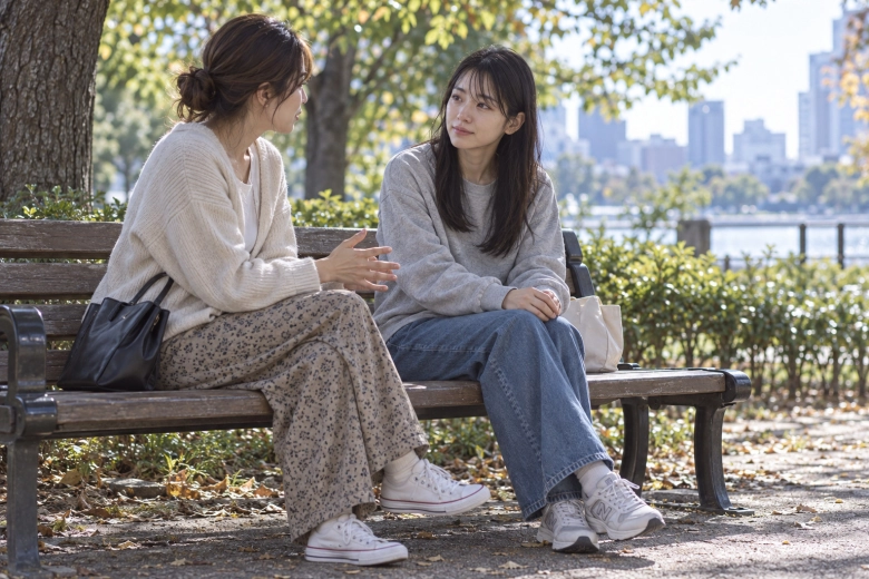 公園のベンチで友人と話す女性